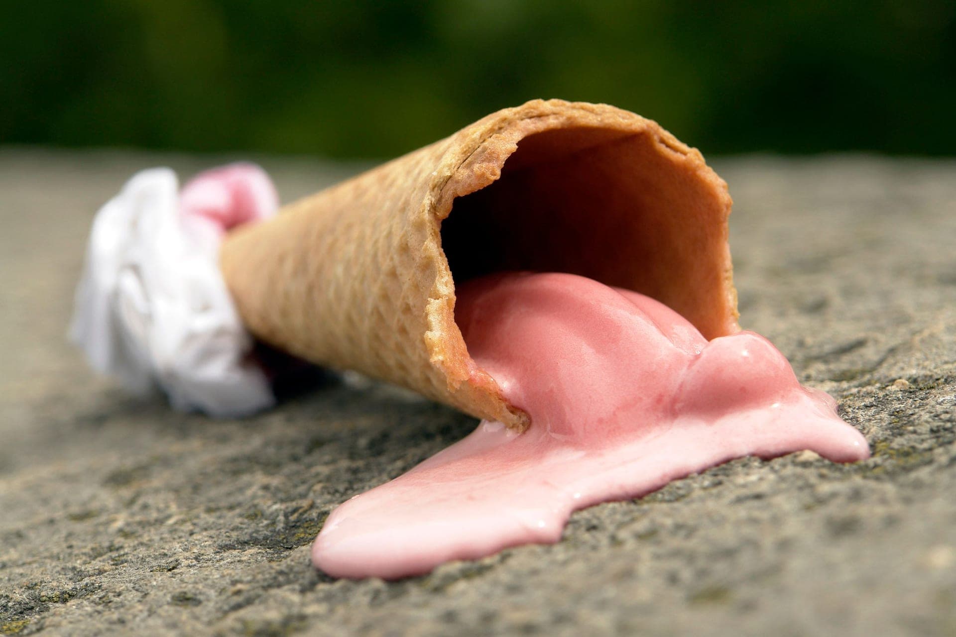 A melting strawberry ice cream cone on a stone surface