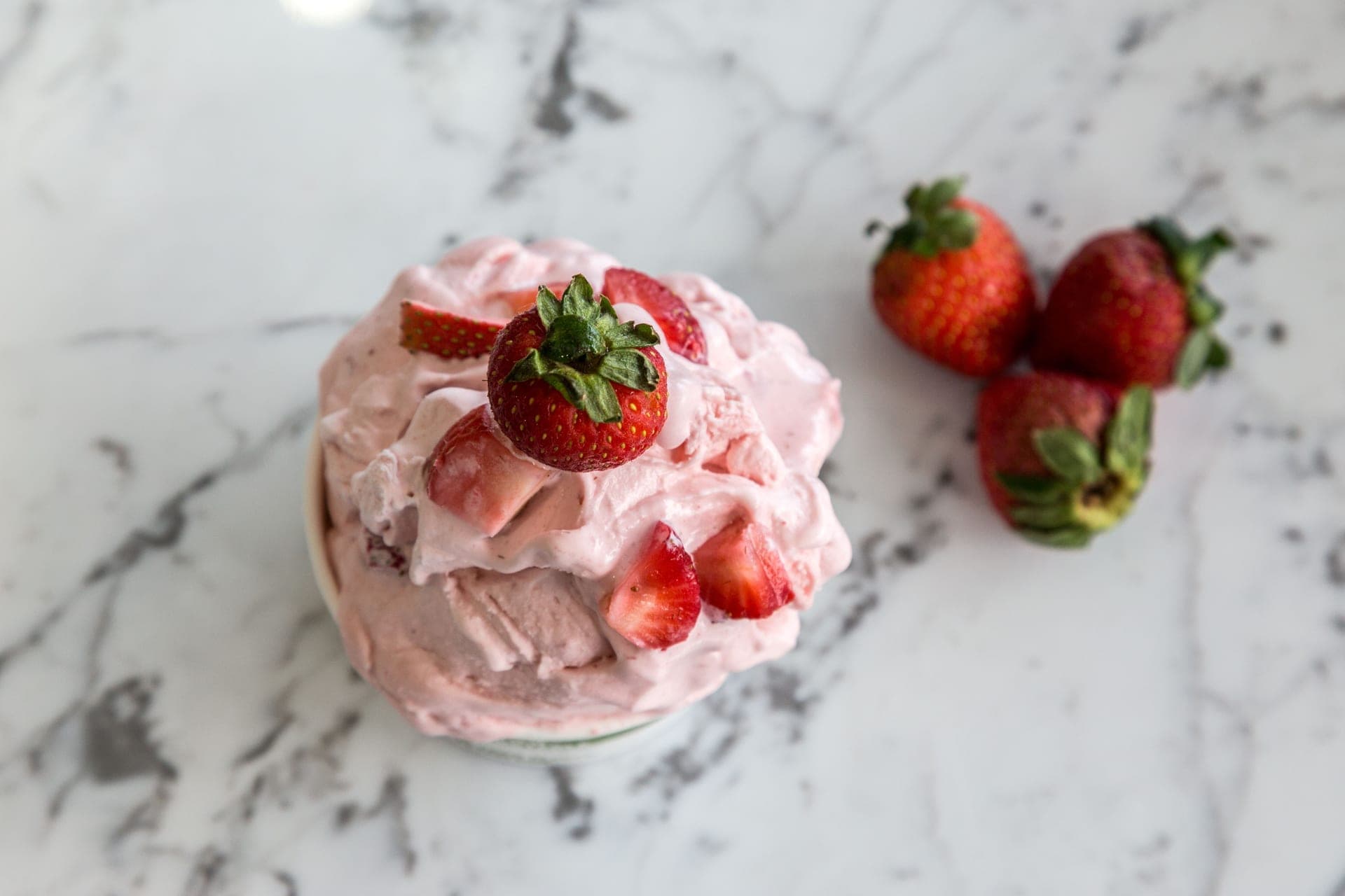 A bowl of homemade strawberry ice cream with fresh strawberries